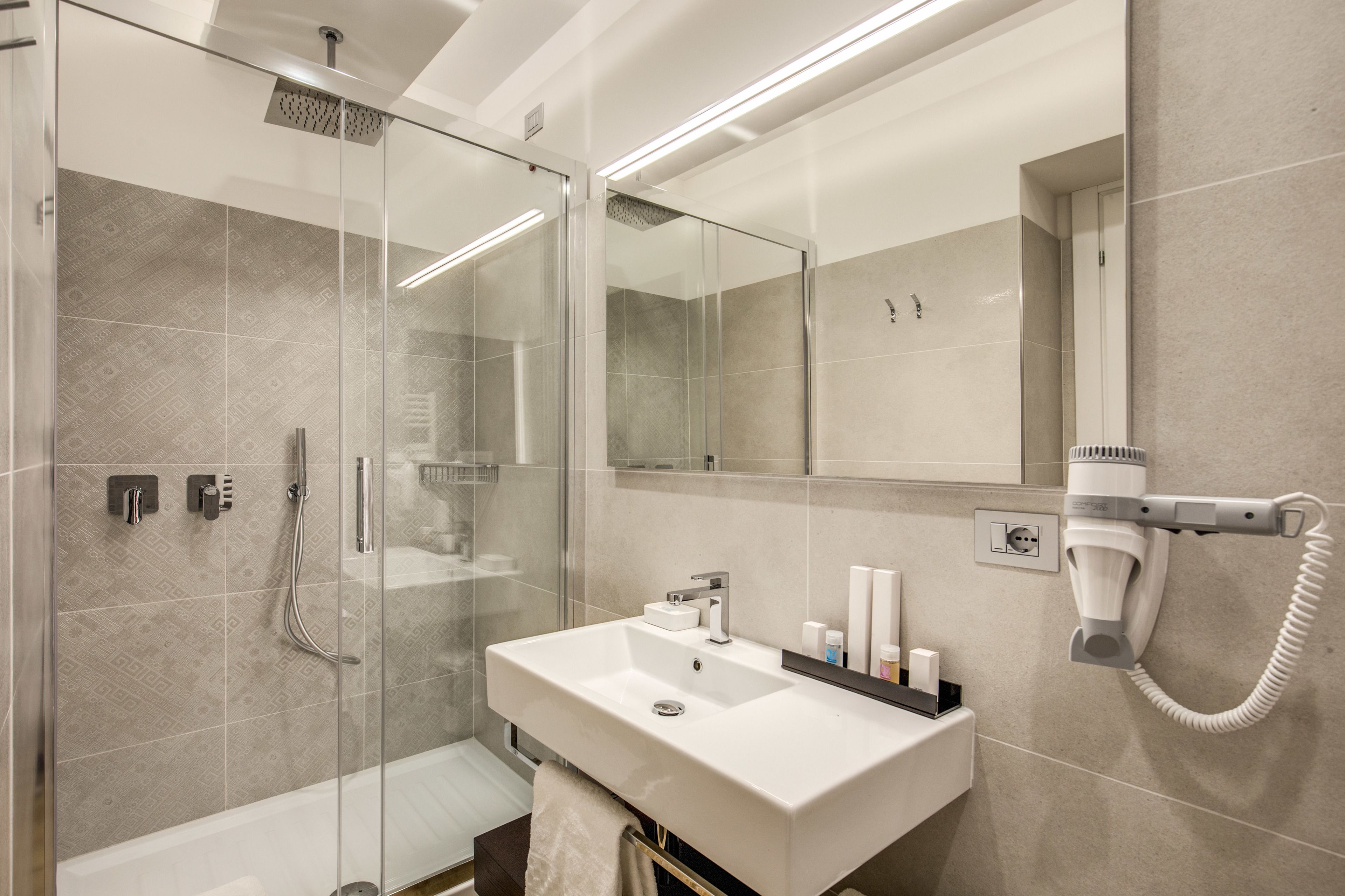 A modern bathroom with a glass-enclosed shower, a white sink, and a hairdryer mounted on the wall.
