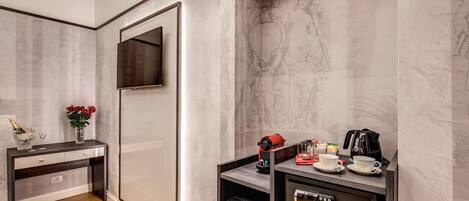 A modern hotel room with a marble wall, a wooden console table, a flat-screen TV, a minibar, and a coffee machine.