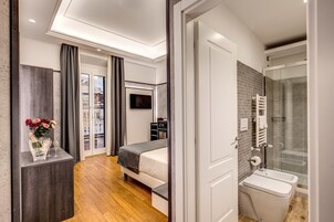 A modern hotel room with a bed, a TV, a minibar, and a bathroom with a shower and toilet.