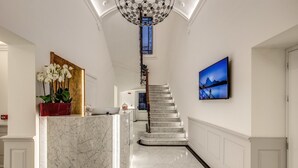Eine prachtvolle Eingangshalle mit einem Marmor-Empfangstresen, einer Treppe und einem großen Gemälde an der Wand.