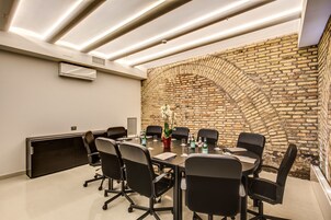 Una sala de conferencias con pared de ladrillo, iluminación moderna y sillas de oficina negras.
