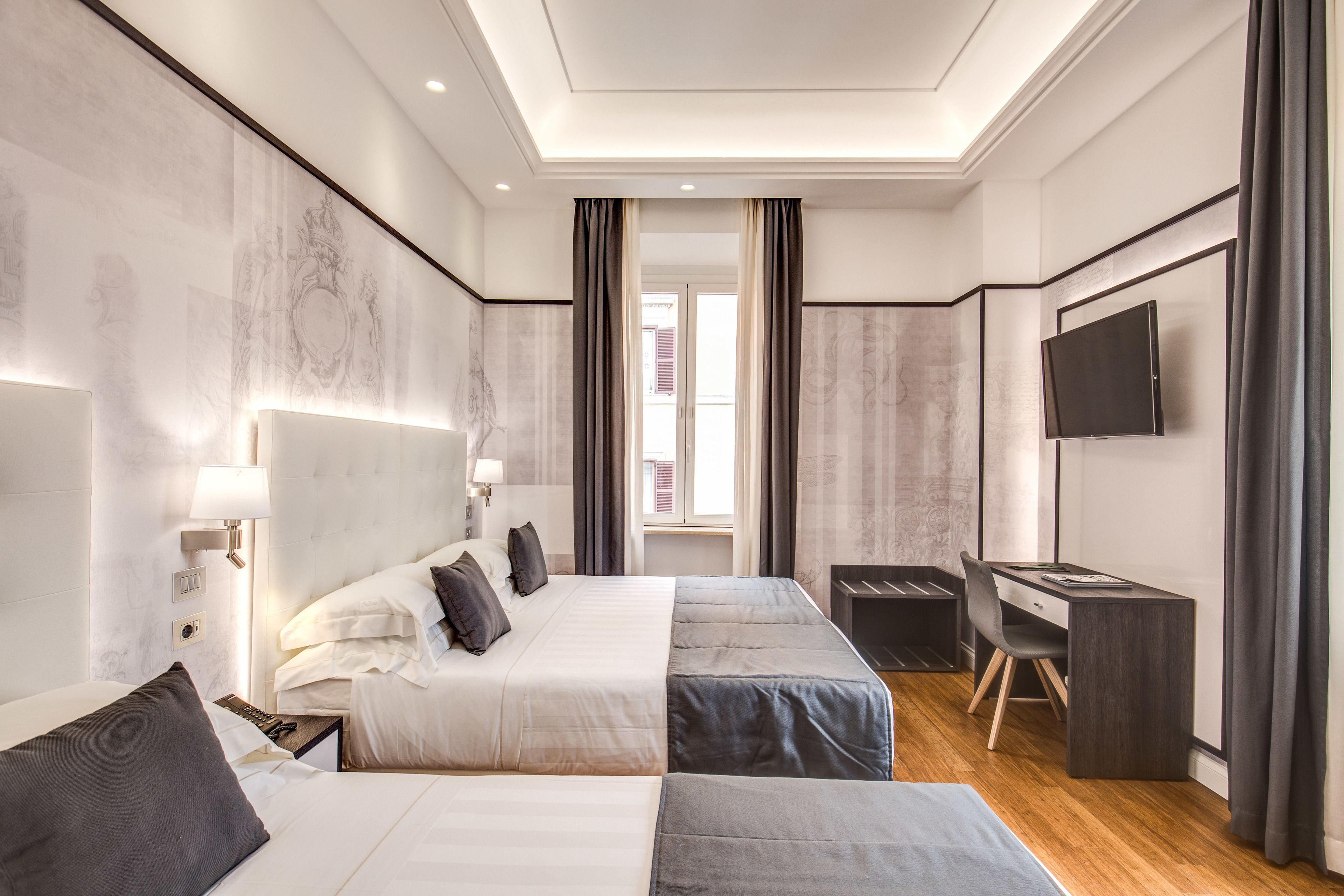 A modern hotel room with two beds, a desk, a TV, and a large window.