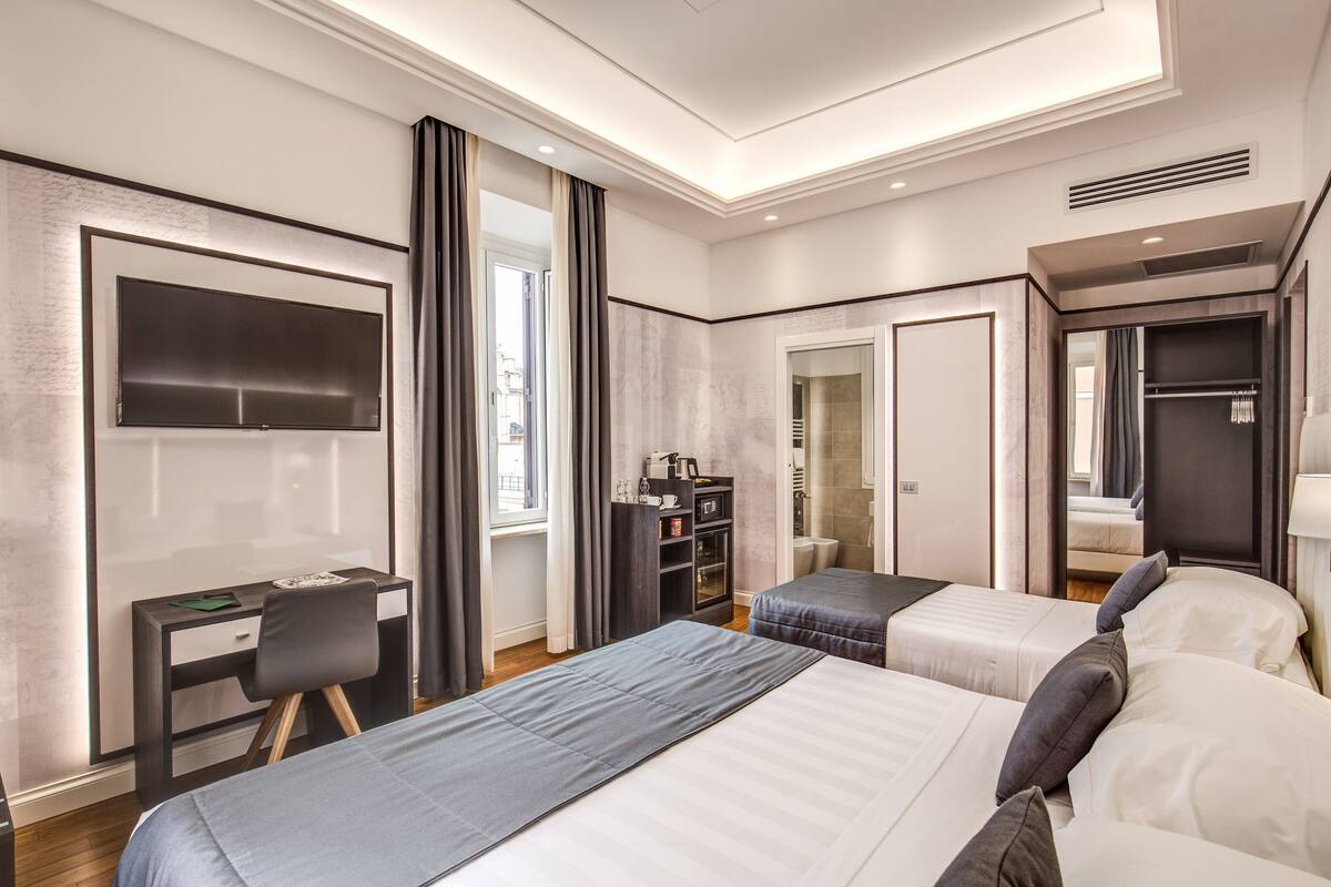 A modern hotel room with two beds, a desk, a TV, and a wardrobe.