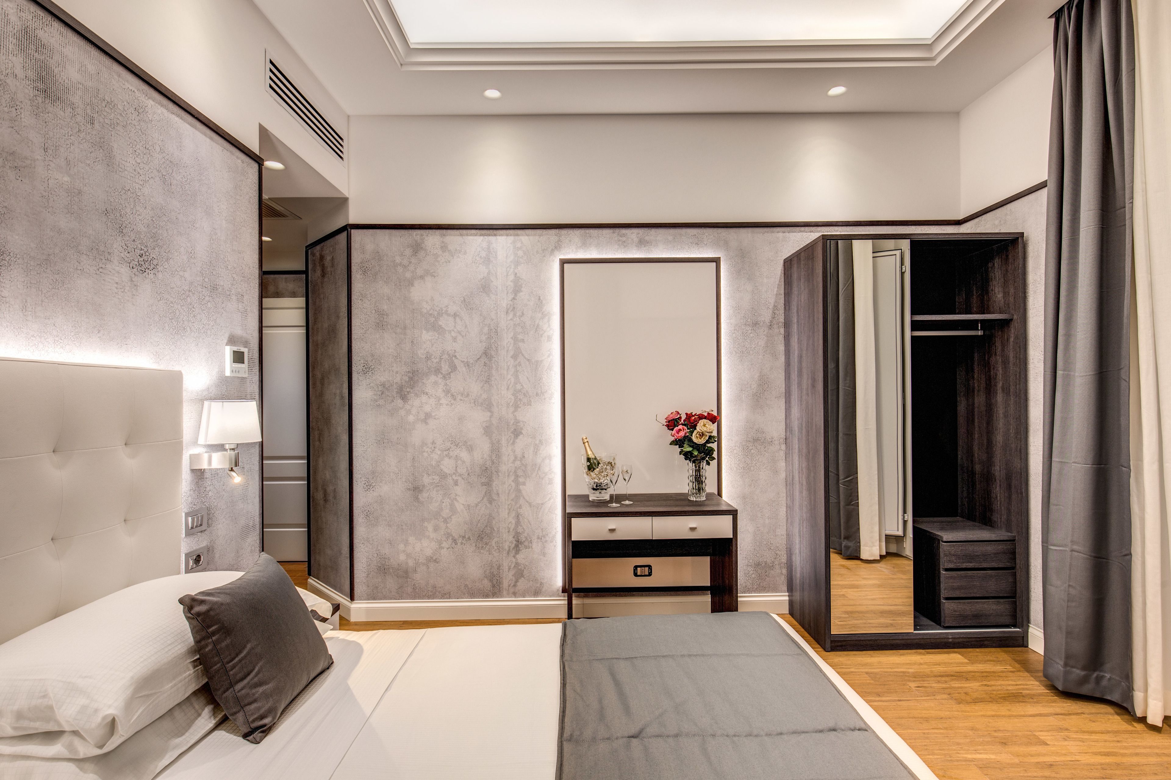 A modern bedroom with a large bed, a bedside table with a lamp, a mirror, and a wardrobe.