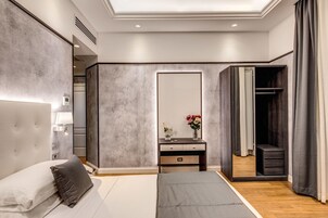 A modern bedroom with a large bed, a bedside table with a lamp, a mirror, and a wardrobe.