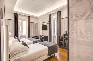A modern hotel room with two beds, a desk, a television, and a minibar.