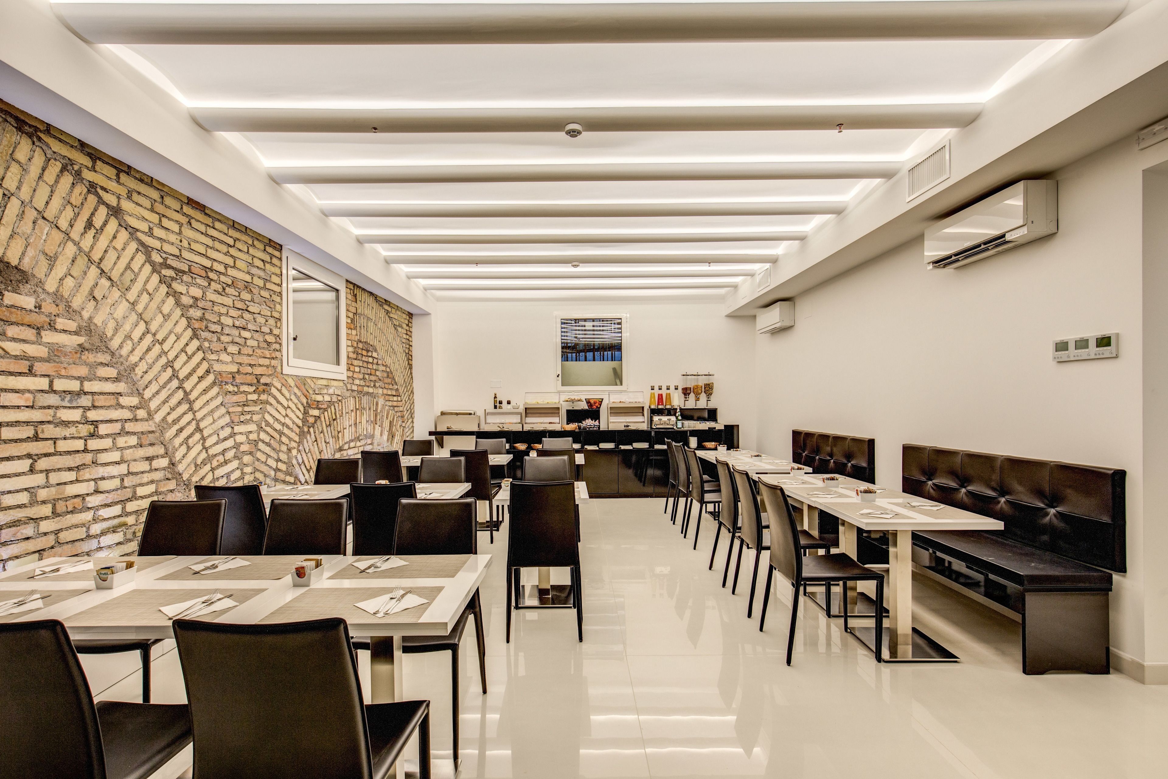 A modern restaurant with a brick wall, long tables, and a high ceiling with recessed lighting.