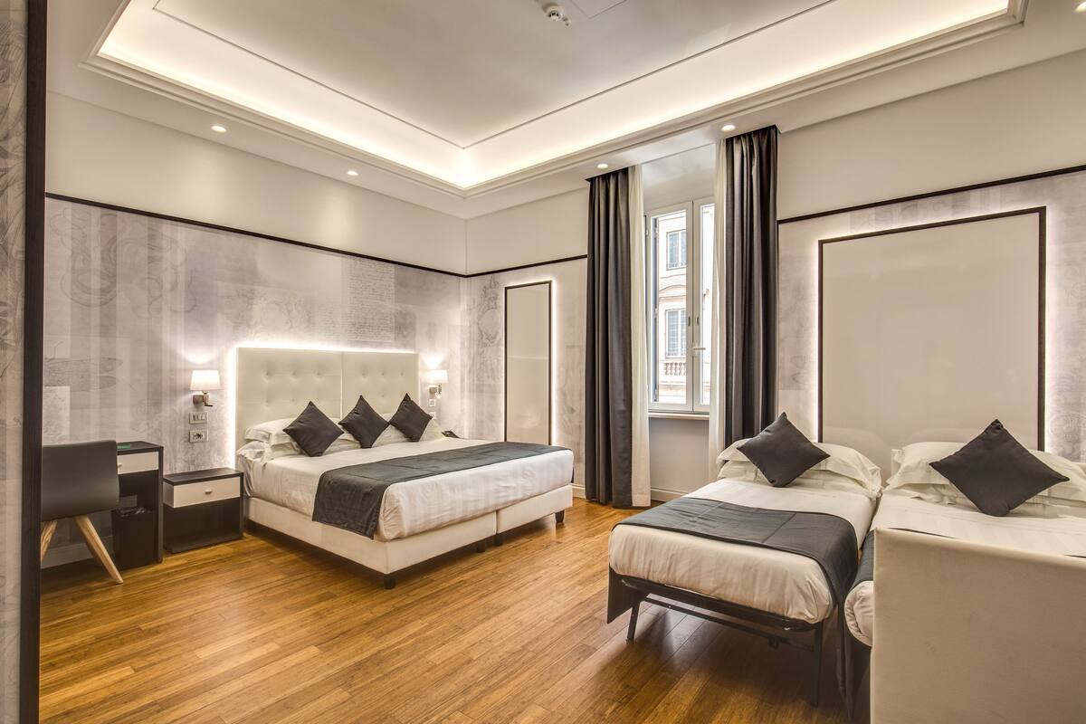 A modern hotel room with a large bed, a smaller bed, a desk, and a chair.