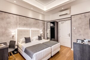 A modern hotel room with a large bed, a desk, and a wardrobe.