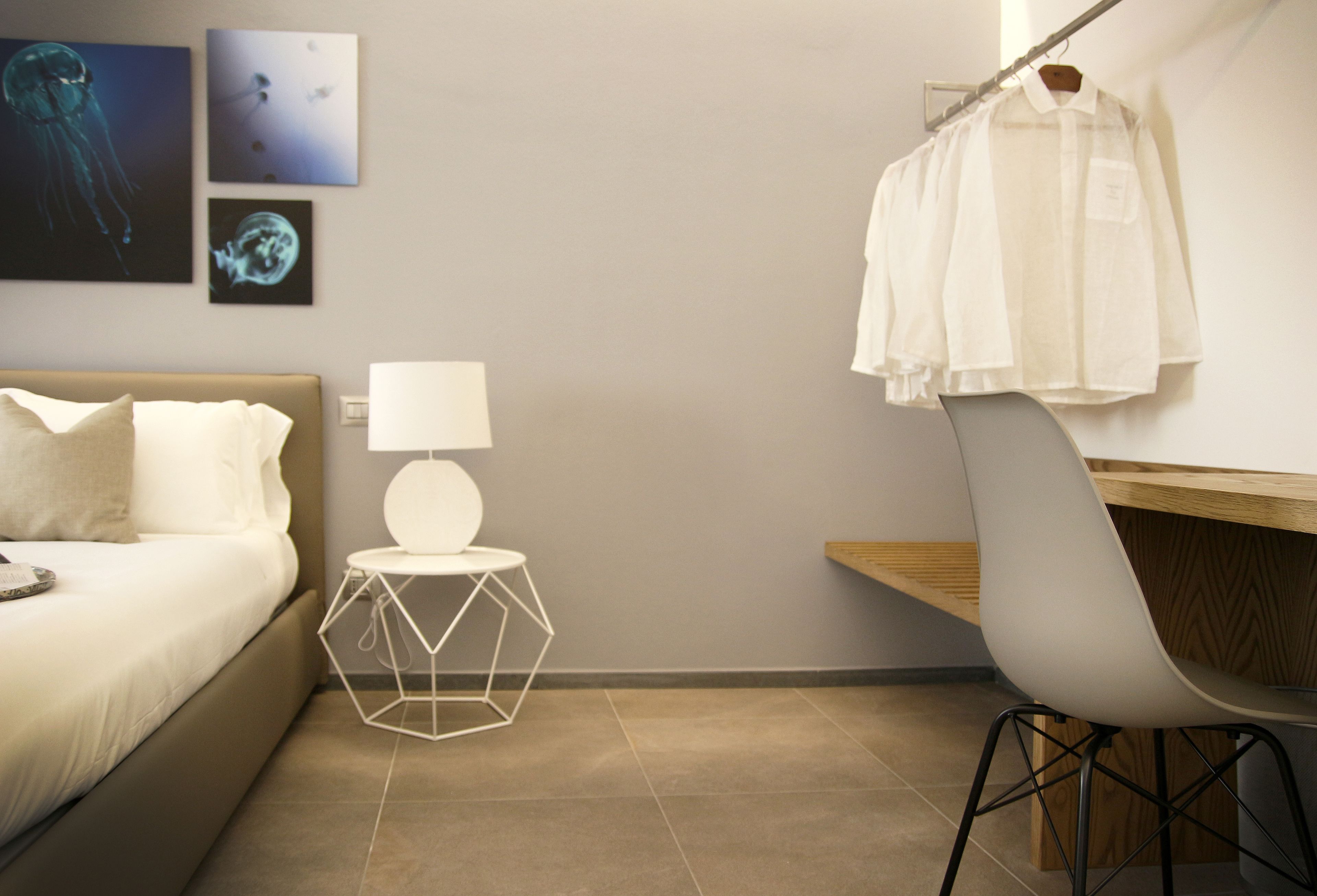 Quarto moderno com cama, mesa de cabeceira com luminária, cadeira e escrivaninha.
