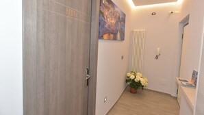 A hallway with a wooden door, a radiator, a potted plant with white flowers, and a painting on the wall.