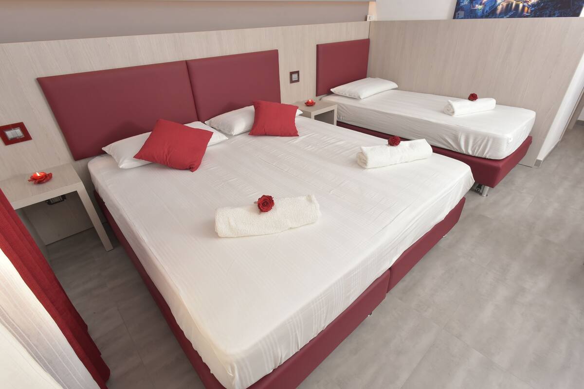 A hotel room with two beds, each with white linens and red accents, and a red headboard.