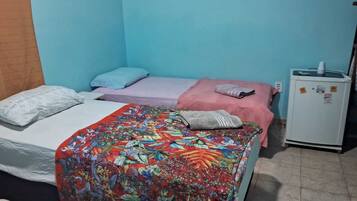 Habitación pequeña y compacta con dos camas individuales, cada una con un edredón de diferente color. A la derecha hay un refrigerador blanco pequeño.