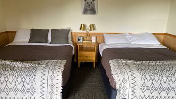 A hotel room with two beds, each with patterned bedspreads and pillows. There is a nightstand with a lamp and a framed picture on the wall above the beds.