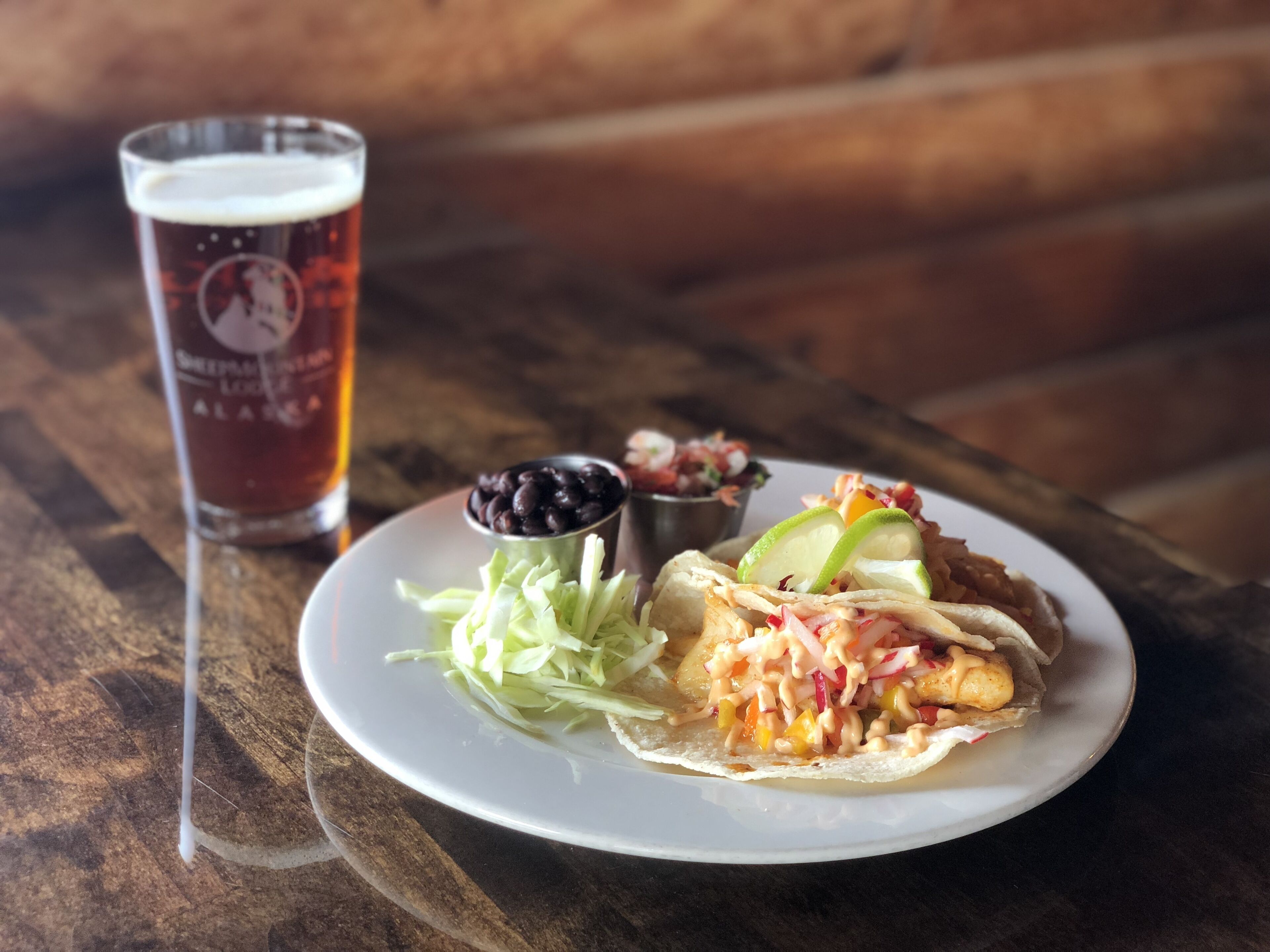 Ein Teller mit einem Taco, einem Bierglas und einer kleinen Schale schwarzer Bohnen.