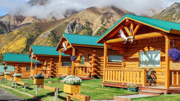 A row of log cabins with green roofs, wooden railings, and flower planters in front. - Sheep Mountain Lodge (Sutton)