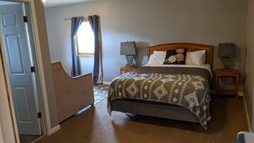 A bedroom with a bed, two bedside tables with lamps, a window with curtains, and a door.