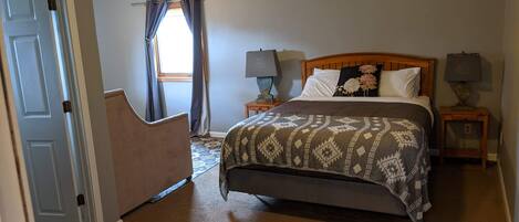 A bedroom with a bed, two bedside tables with lamps, a window with curtains, and a door.