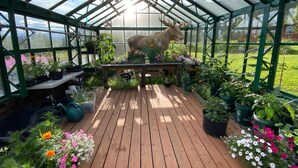 A greenhouse with a wooden deck, various potted plants, and a large deer sculpture. - Sheep Mountain Lodge (Sutton)