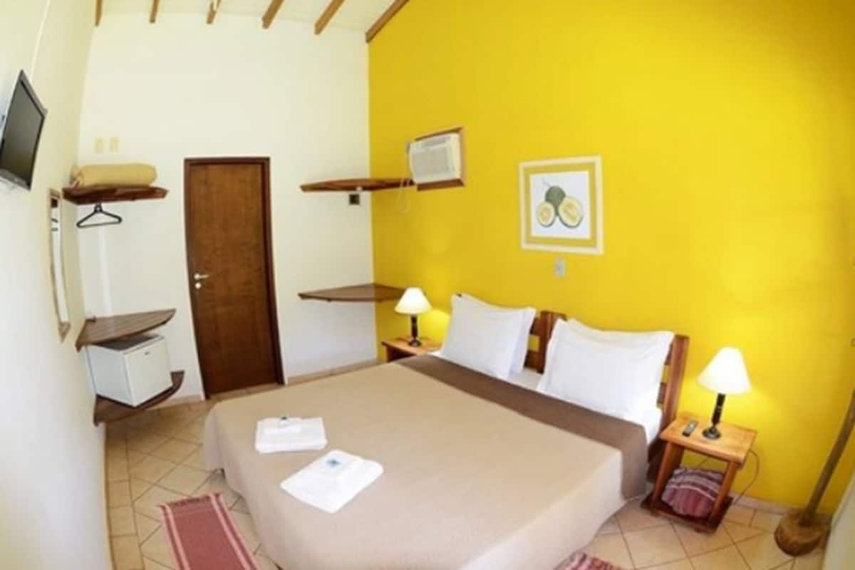 Un dormitorio con cama, mesitas de noche, televisor, escritorio y puerta.