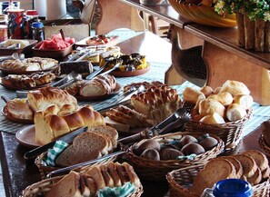 A buffet table with various breads, pastries, and a bowl of fruit. - Hotel Fazenda Jacaúna (Brotas)