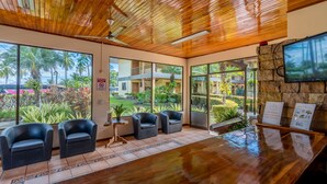 A reception area with a wooden ceiling, large windows, and a TV mounted on a stone wall. - Hotel Manuel Antonio (Quepos)