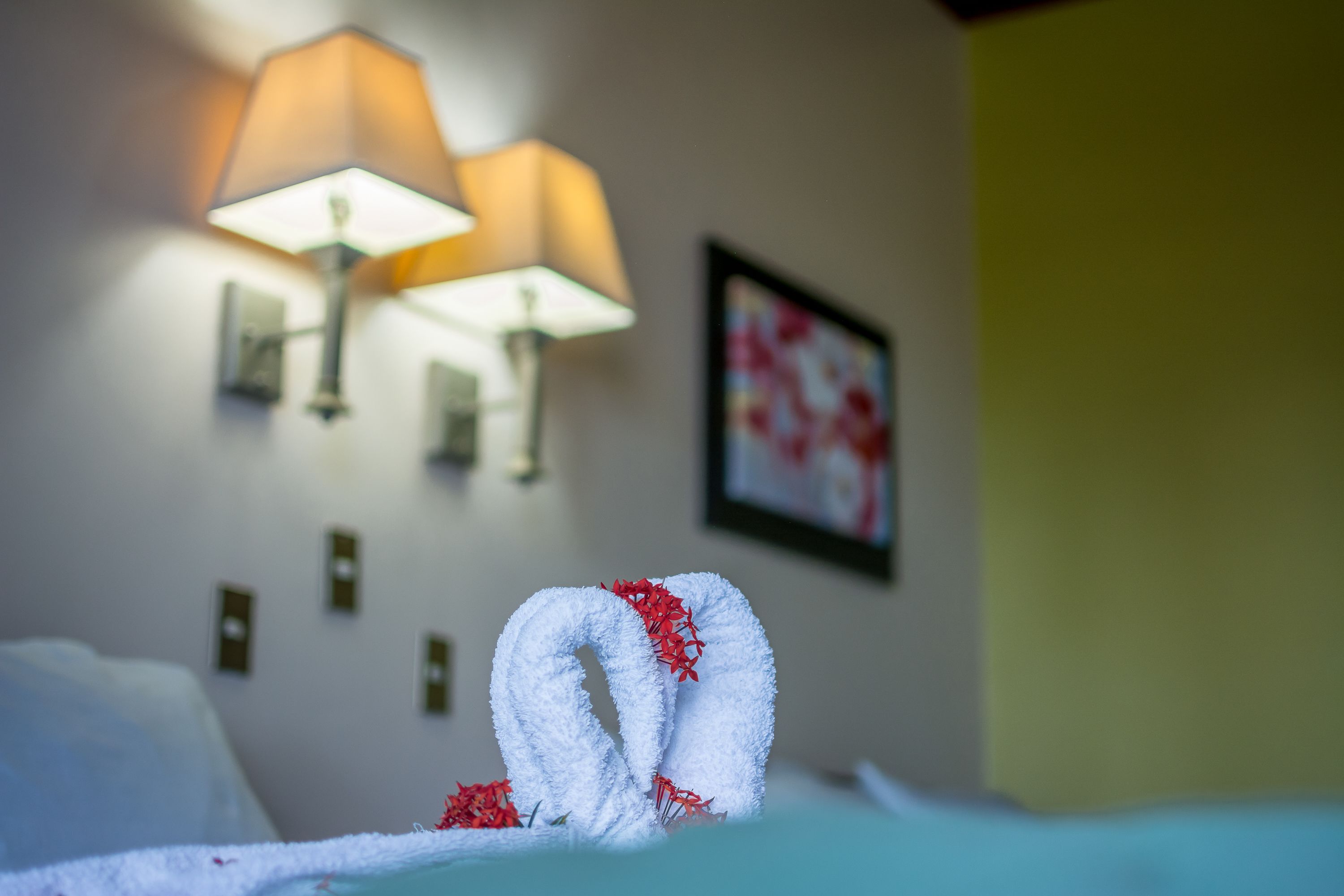 A hotel room with a bed, two wall-mounted lamps, and a framed picture on the wall.
