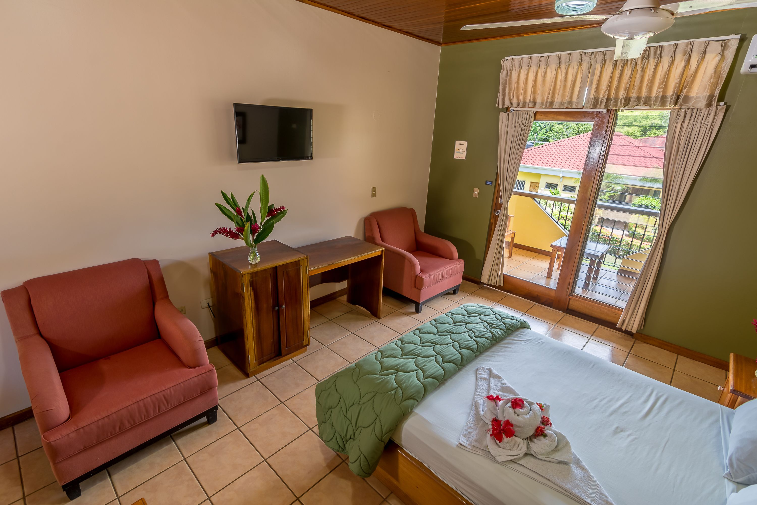 A hotel room with a bed, two chairs, a desk, a TV, and a window with curtains.