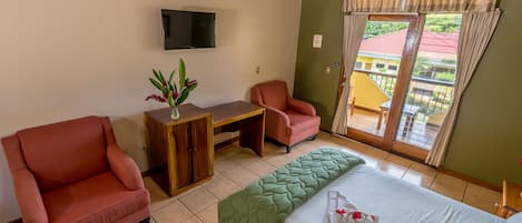 A hotel room with a bed, two chairs, a desk, a TV, and a window with curtains.