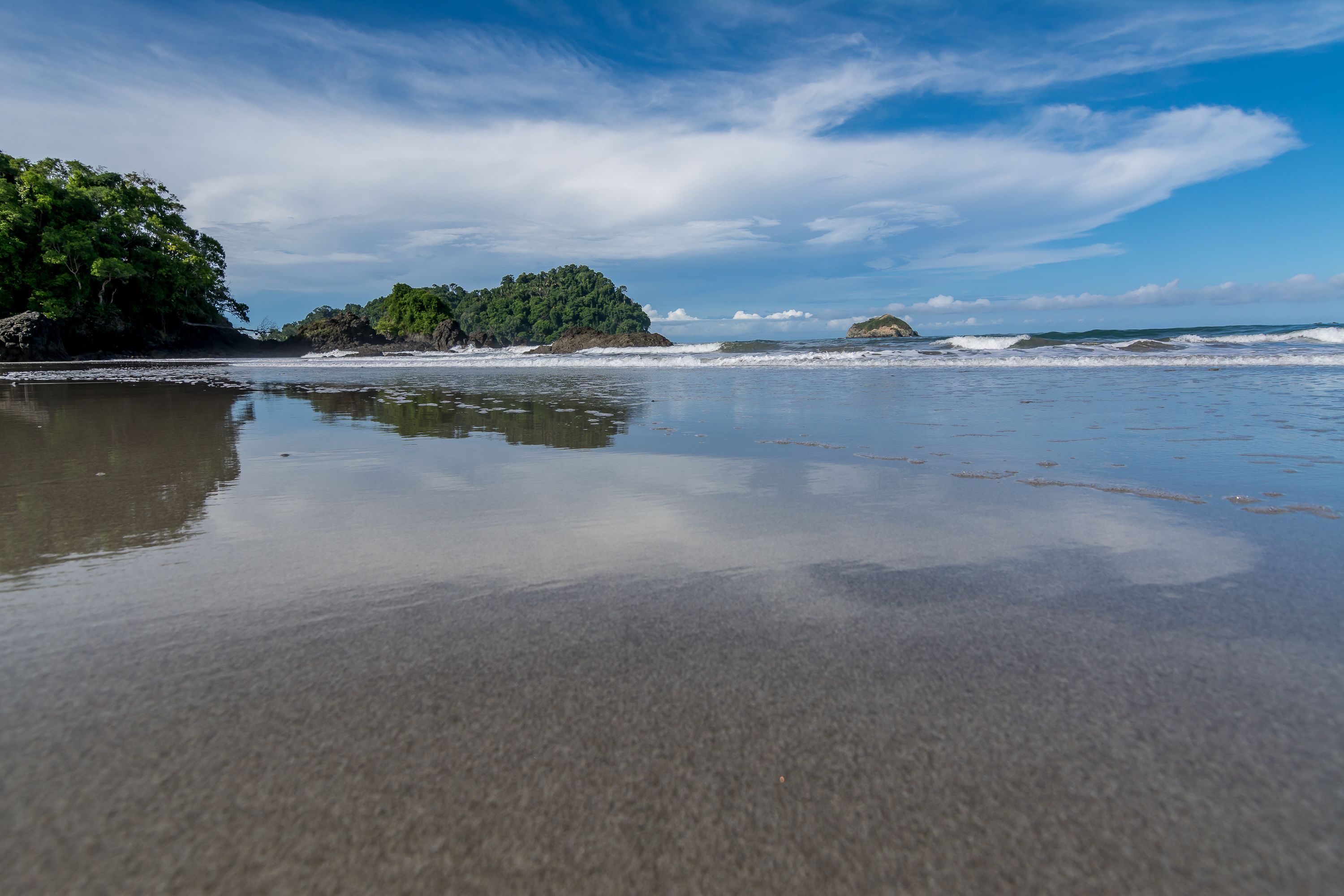 A beach with calm waters, a sandy shore, and a small island with dense vegetation.