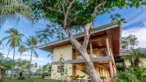 A two-story house with a balcony, surrounded by tropical vegetation and palm trees. - Hotel Manuel Antonio (Quepos)