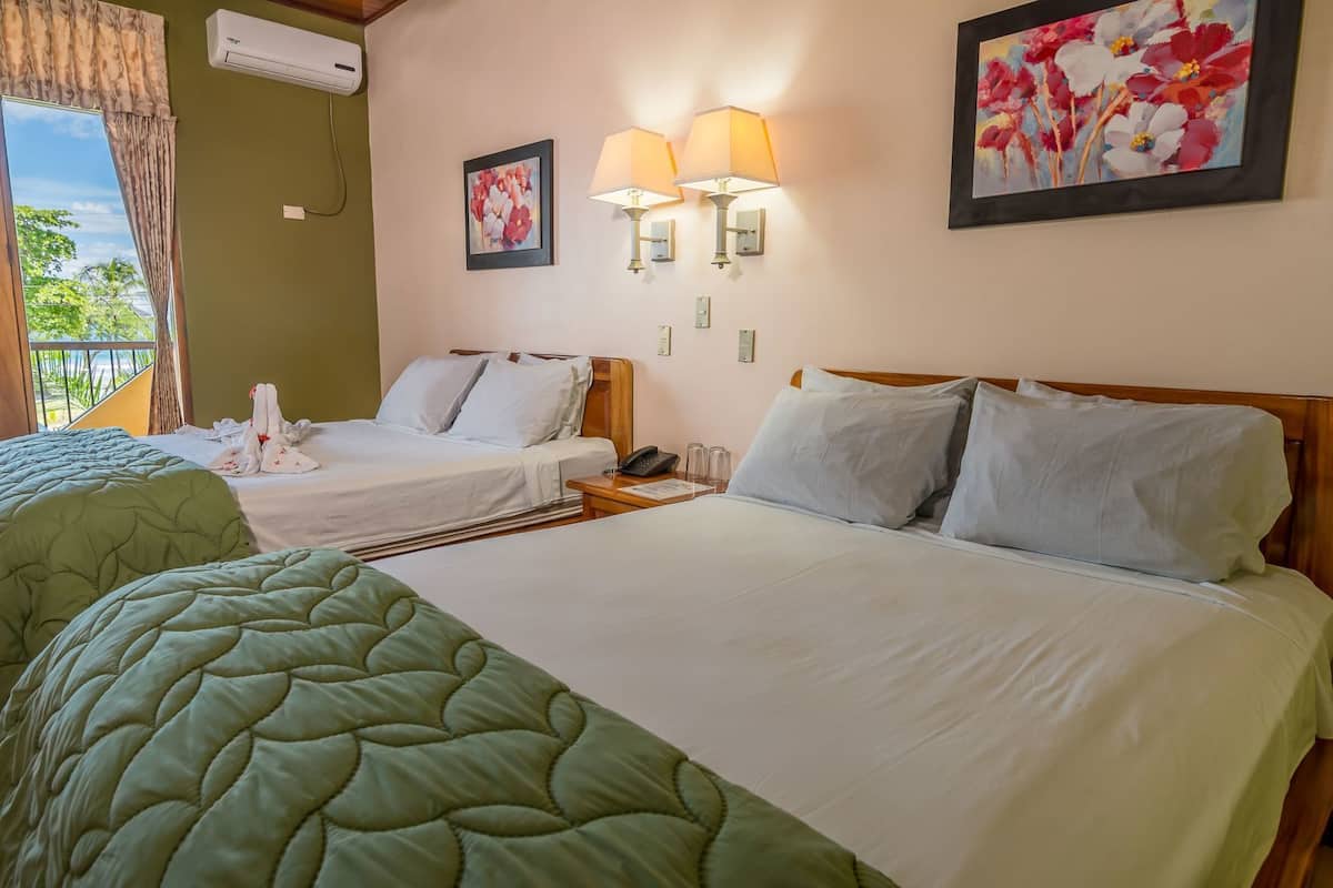 A hotel room with two beds, a balcony, and artwork on the walls.