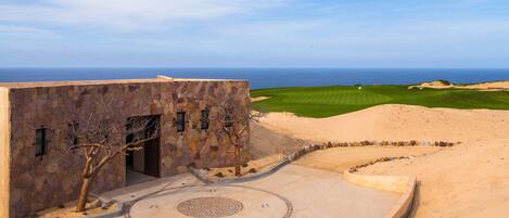 Un edificio de piedra con un patio circular y vistas a un campo de golf y al océano.