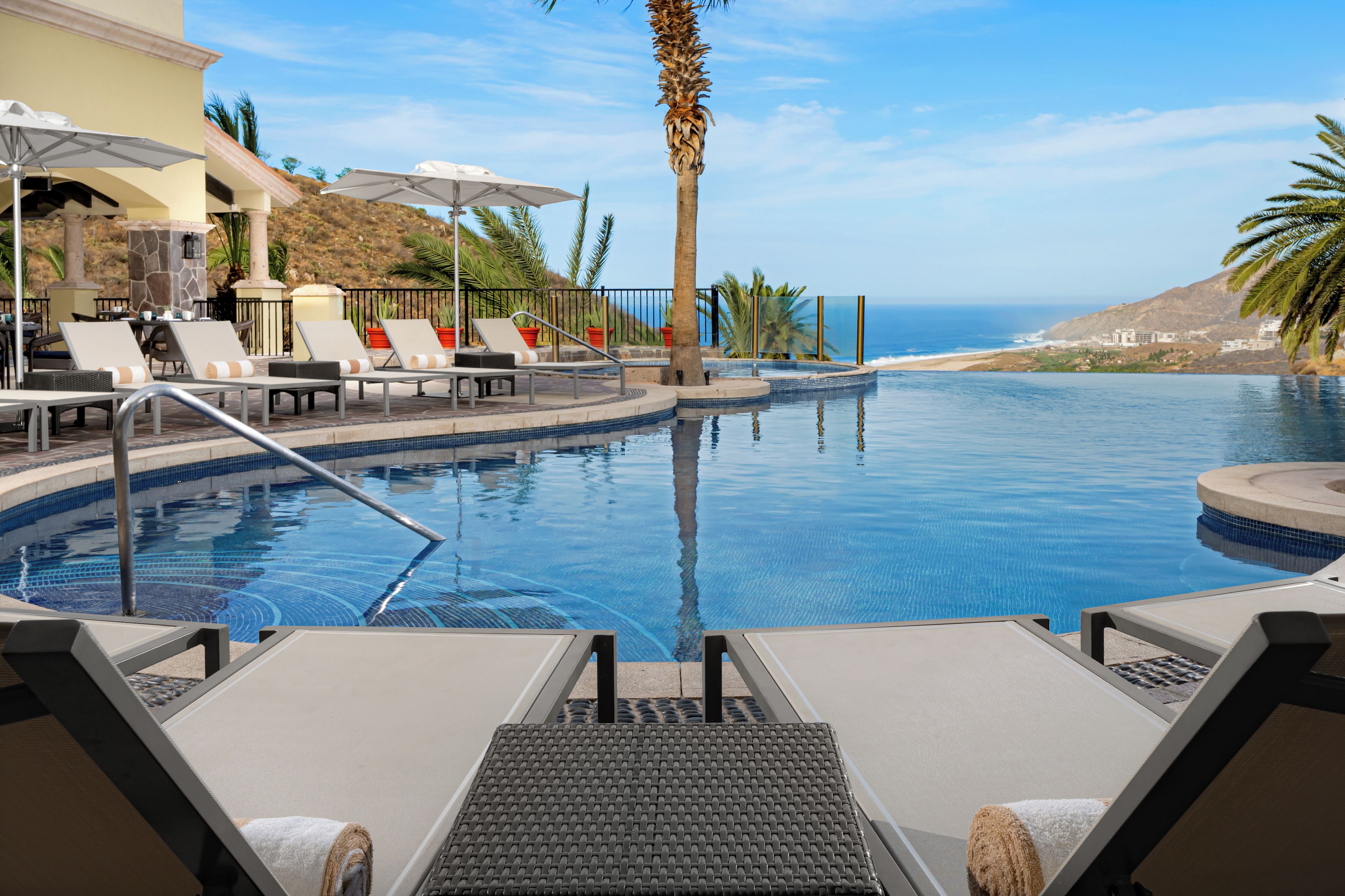 A poolside area with lounge chairs, a palm tree, and a view of the ocean.
