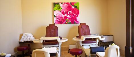 Una habitación con dos sillones de masaje, una mesita con una toalla y un cuadro de flores en la pared.