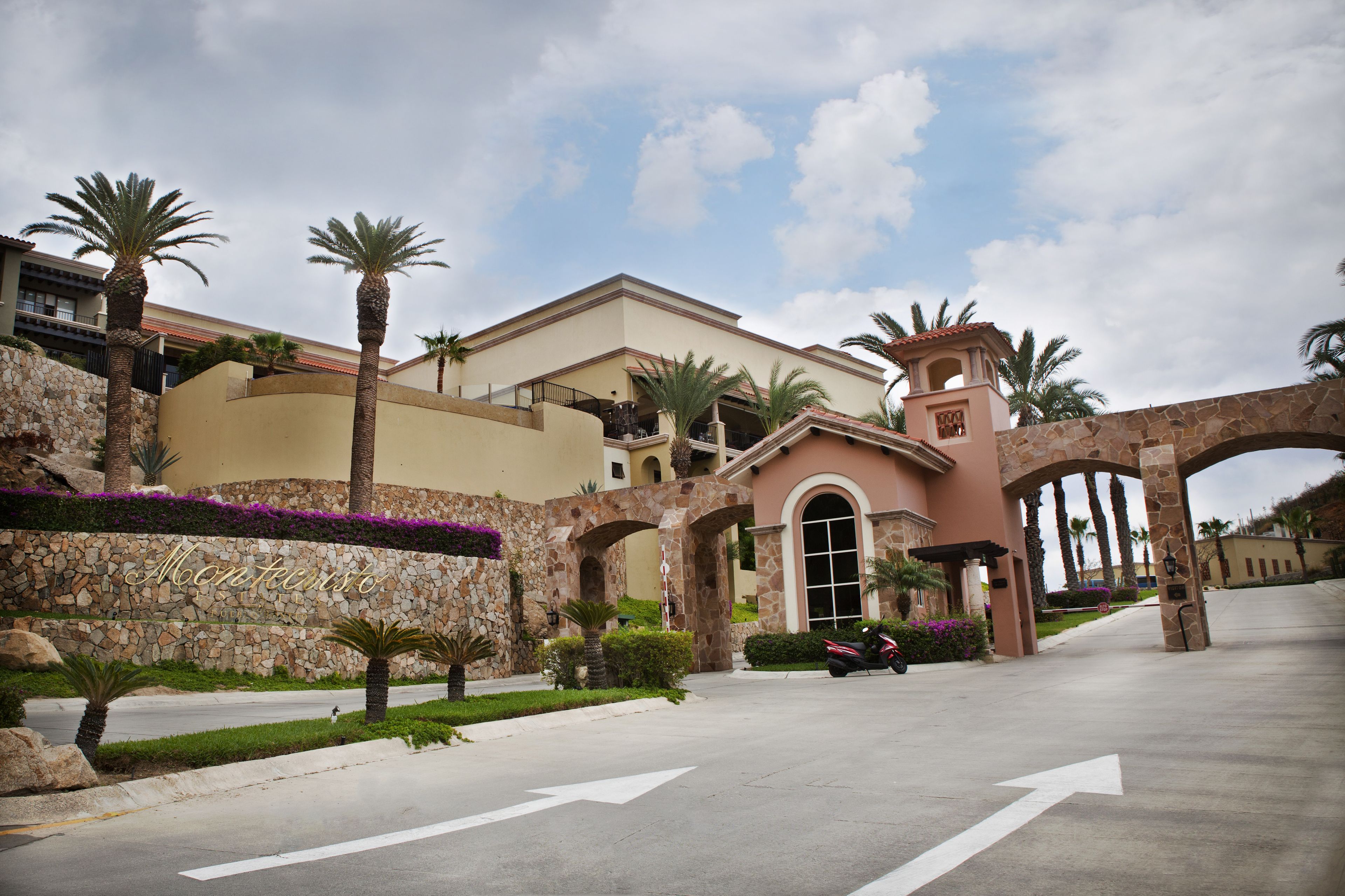 A hotel entrance with a stone wall, palm trees, and a clear sky.