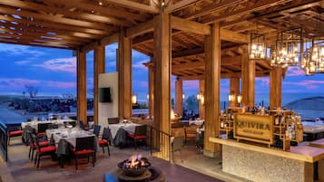 An outdoor dining area with tables and chairs, a bar with a sign reading 'QUIVIRA GOLF CLUB', and a fire feature.