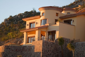 Une maison à plusieurs étages, dotée d’une façade en pierre, de nombreux balcons et surplombant un paysage montagneux.