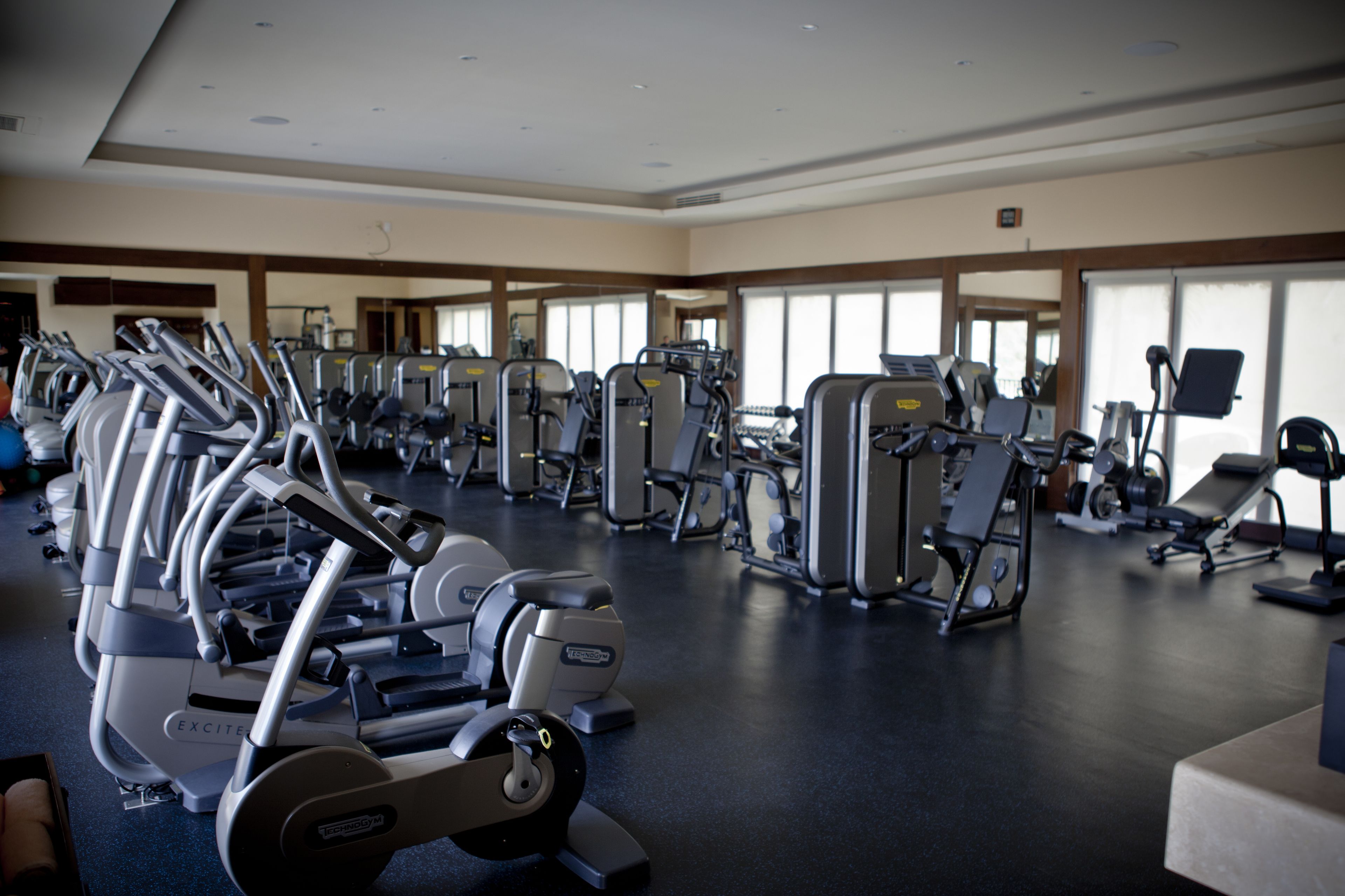 Un gimnasio con diversas máquinas de ejercicio, incluyendo cintas de correr y máquinas de pesas, dispuestas en filas.