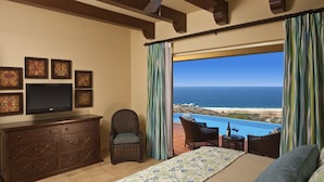 A bedroom with a large bed, a TV on a wooden dresser, wicker chairs, and a view of the ocean. - Quivira Los Cabos Condos & Homes - Vacation Rentals (Cabo San Lucas)