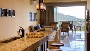 A modern kitchen with a granite countertop, bar stools, and a view of the mountains. - Quivira Los Cabos Condos & Homes - Vacation Rentals (Cabo San Lucas)