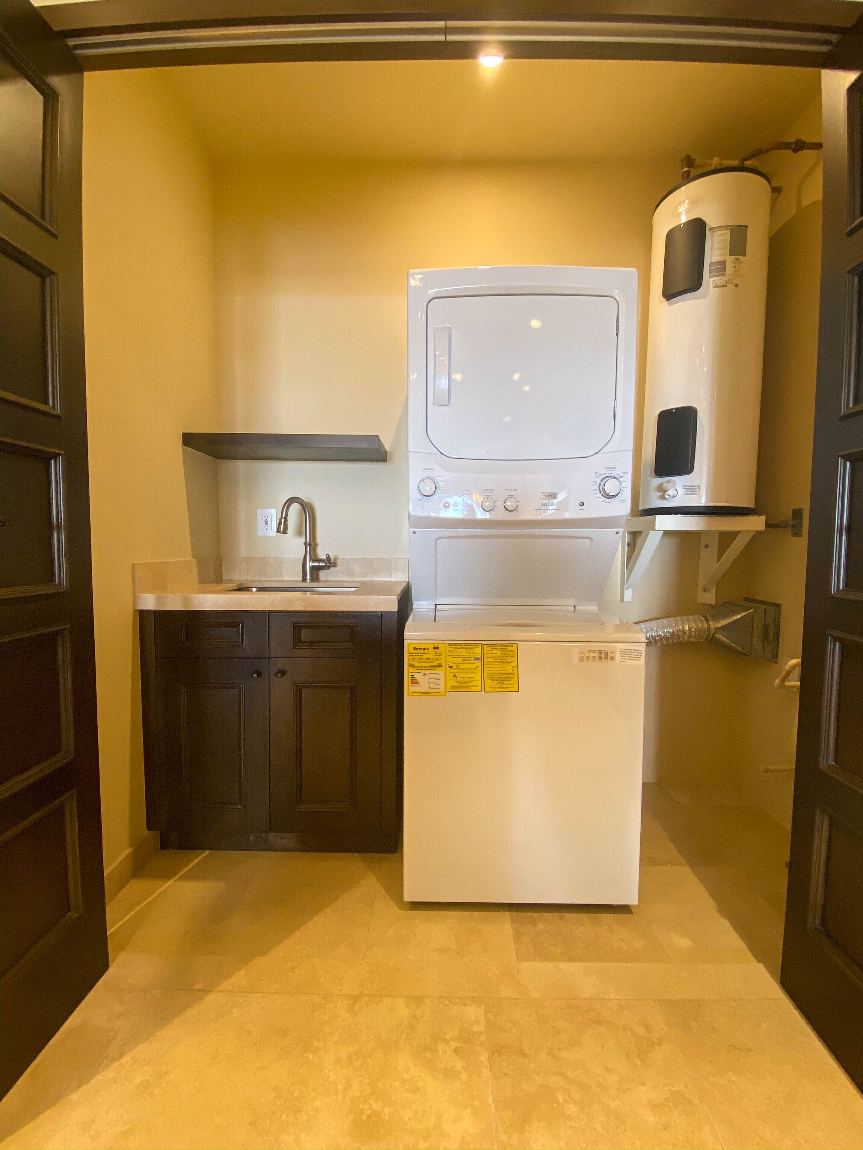 A compact kitchen with a built-in washer and dryer, a sink, and dark wooden cabinets.