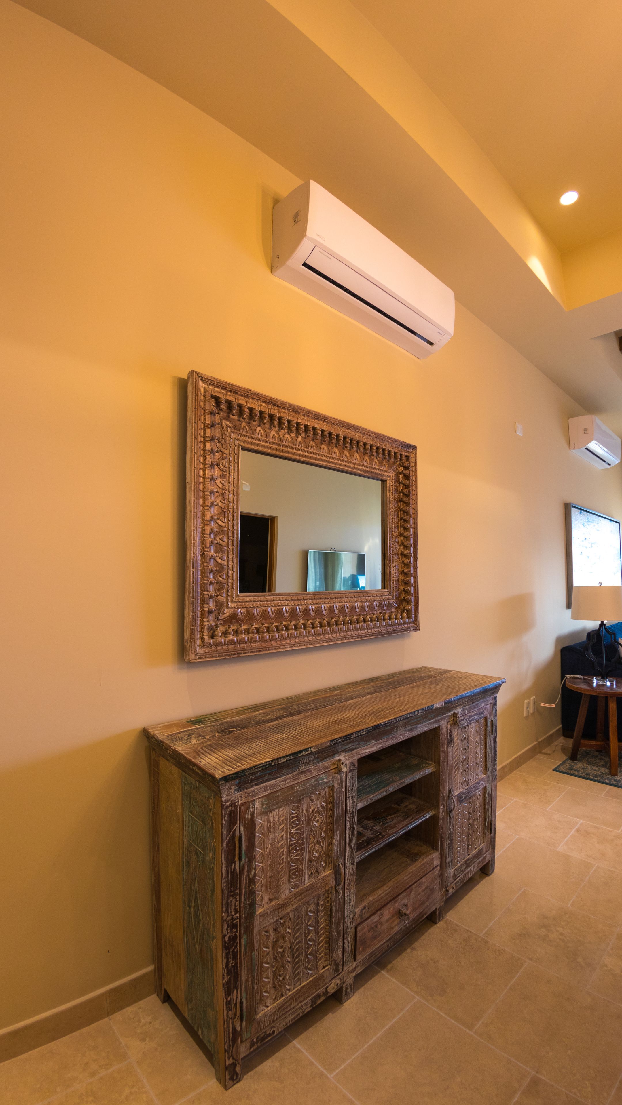 A room with a large ornate mirror, a wooden cabinet, and an air conditioning unit on the wall.