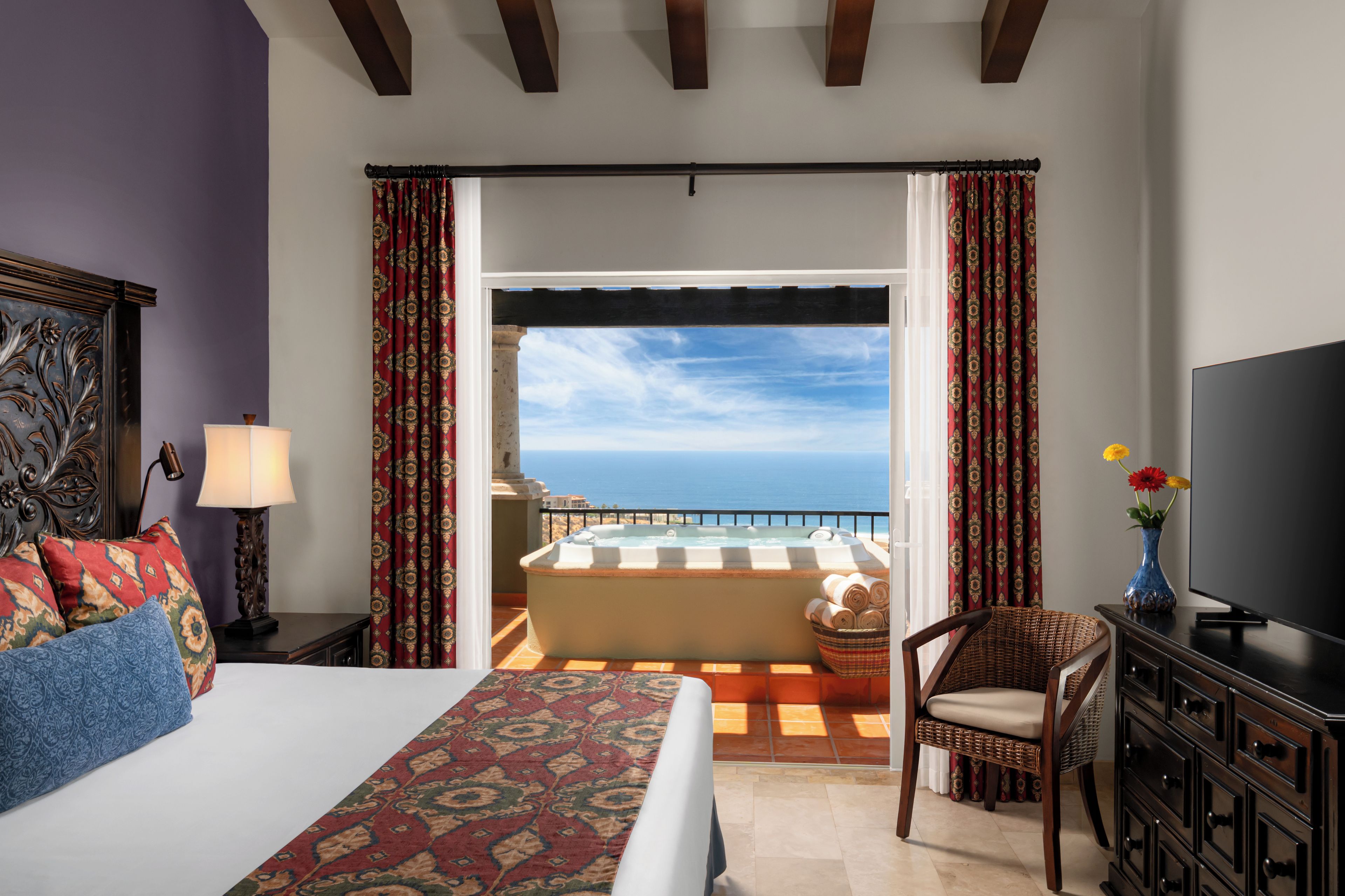 Ein Hotelzimmer mit Bett, Schreibtisch mit Fernseher, Stuhl, Balkon mit Whirlpool und Meerblick.
