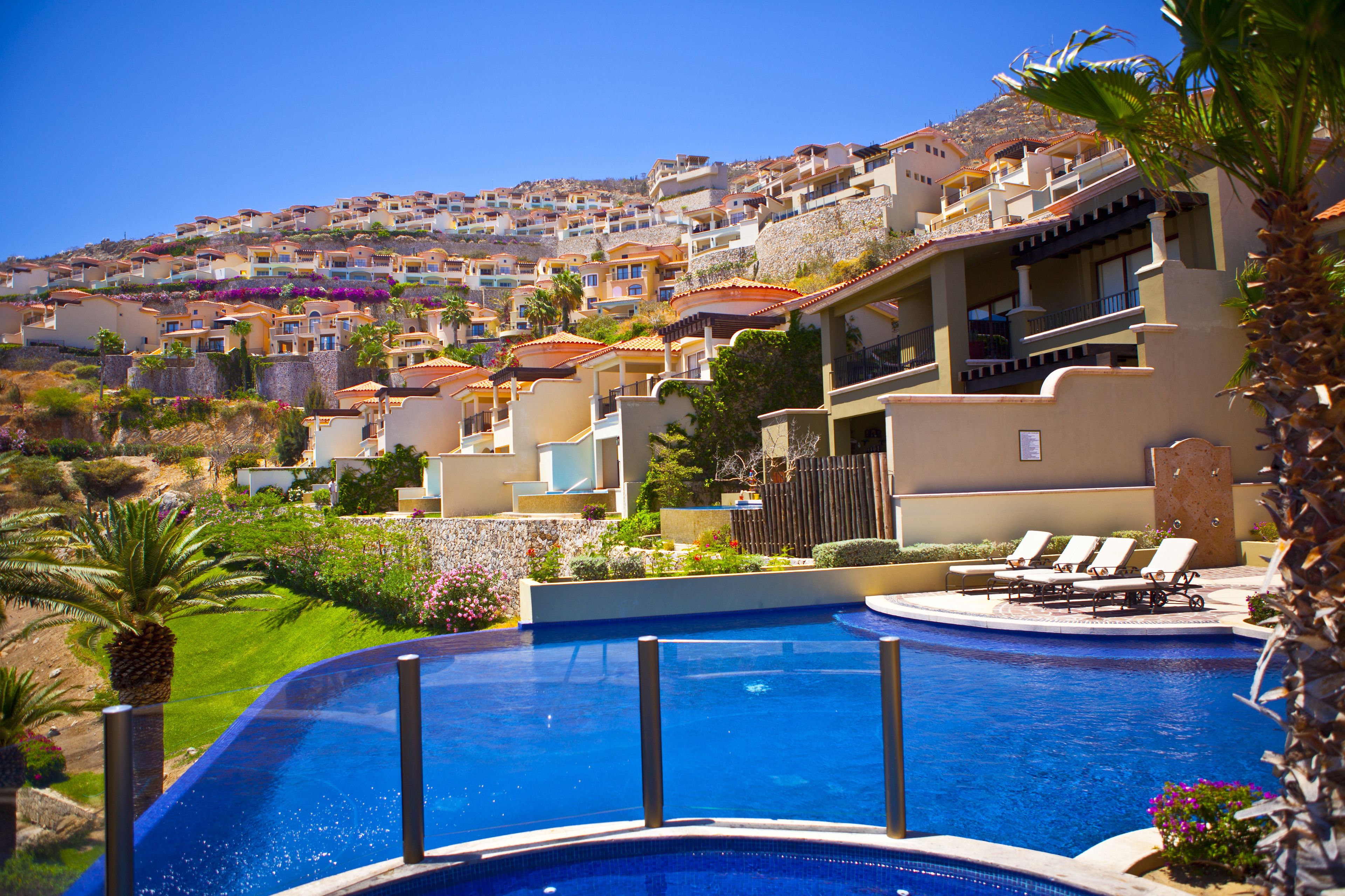 A resort with a swimming pool, lounge chairs, and a view of hillside buildings.