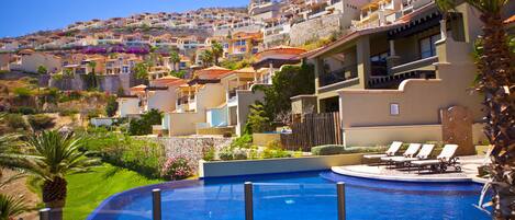 A resort with a swimming pool, lounge chairs, and a view of hillside buildings.