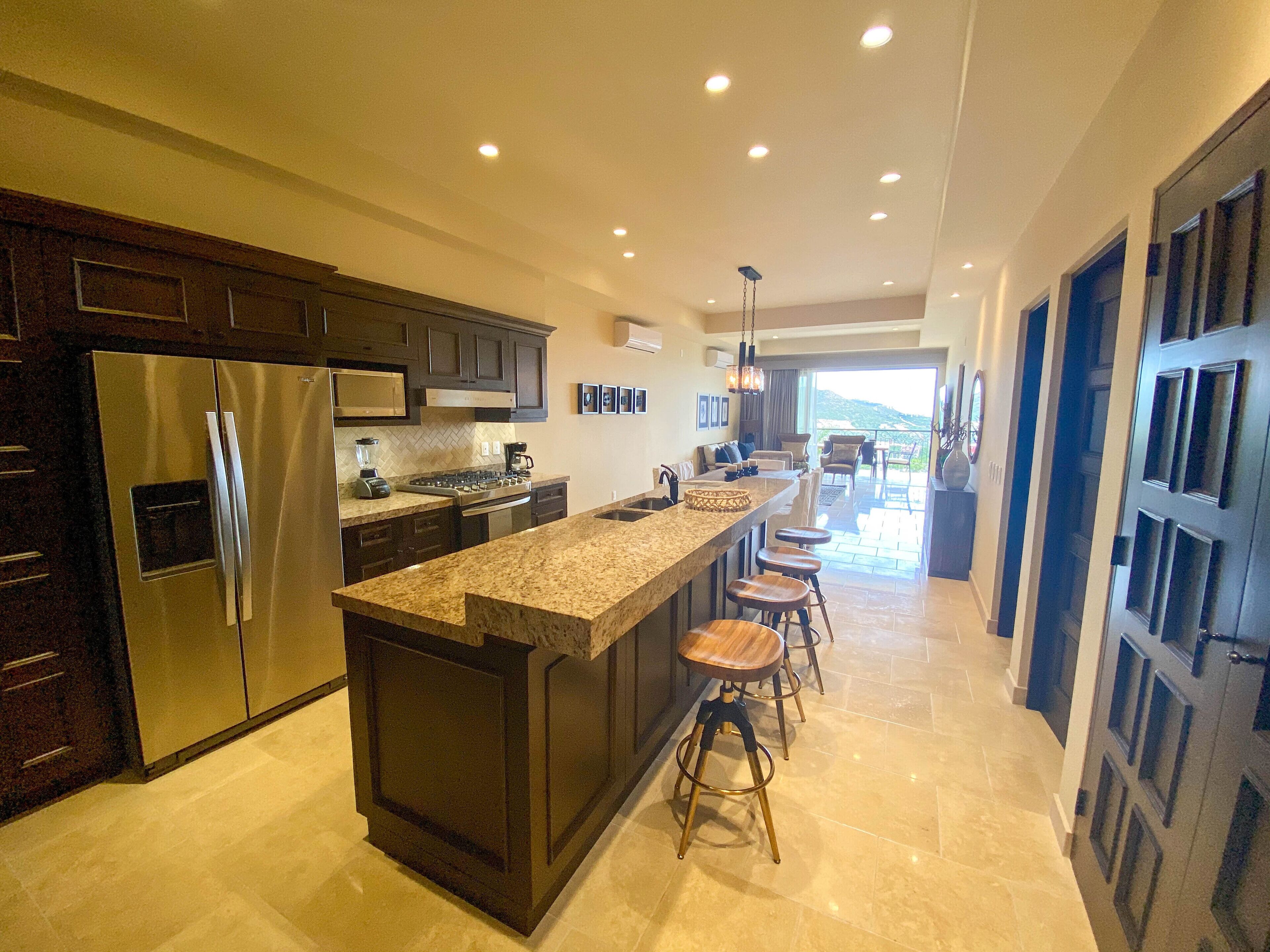 A modern kitchen with dark cabinetry, stainless steel appliances, and a central island with stools.