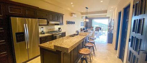 A modern kitchen with dark cabinetry, stainless steel appliances, and a central island with stools.