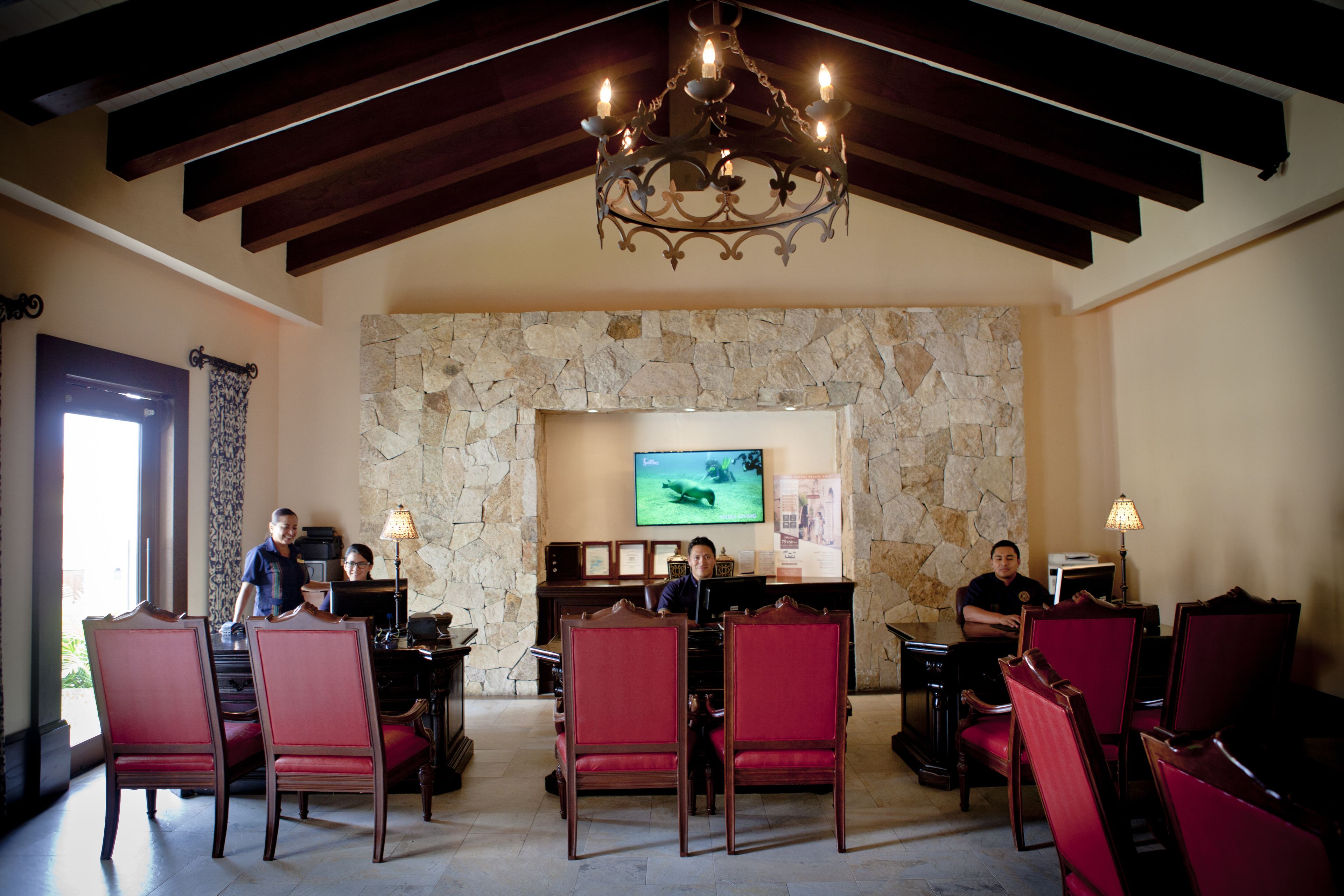 A lobby with a stone fireplace, red upholstered chairs, a chandelier, and a television screen.