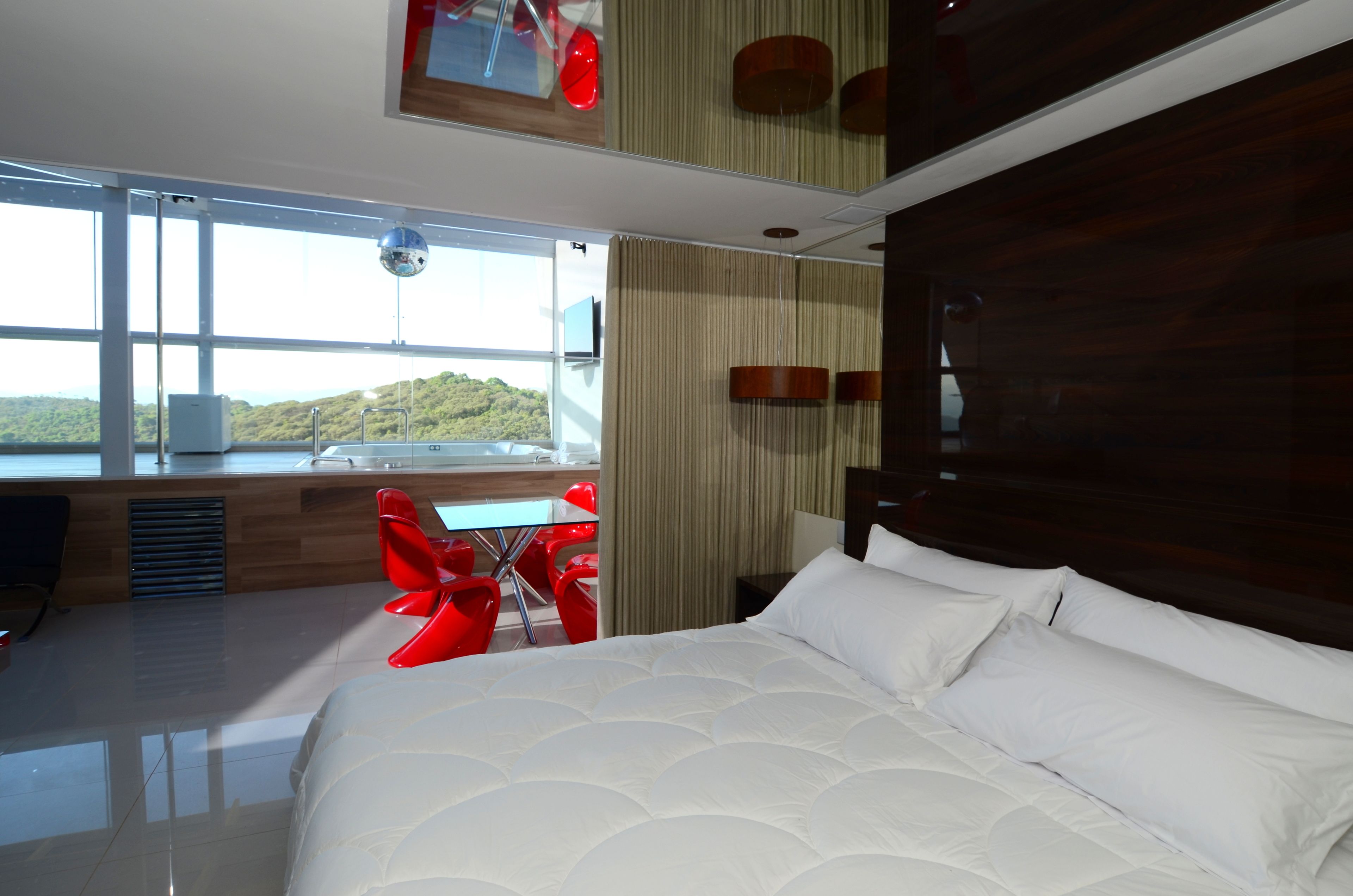 Ett modernt hotellrum med en stor säng, en matplats med röda stolar och utsikt över kullarna.